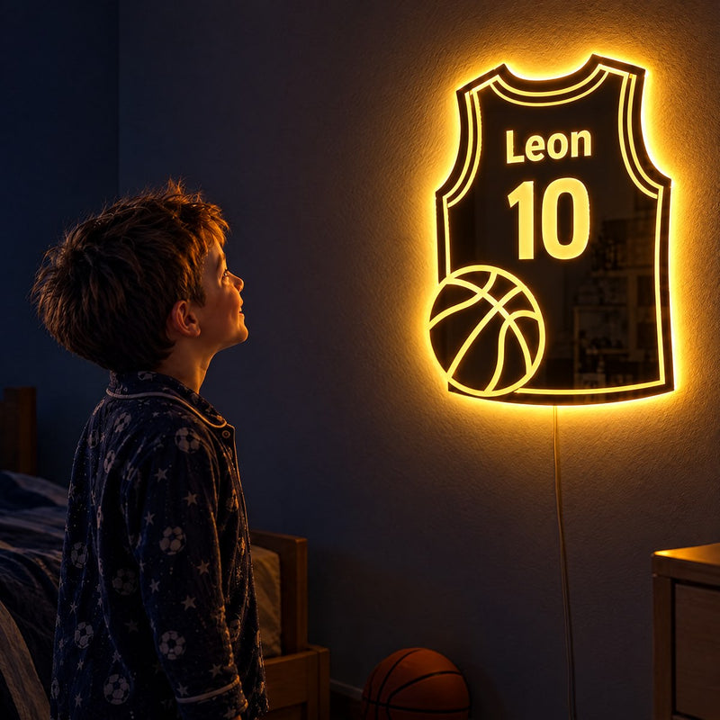 A boy in pajamas gazes in wonder at his warm-glowing basketball jersey mirror with name and number